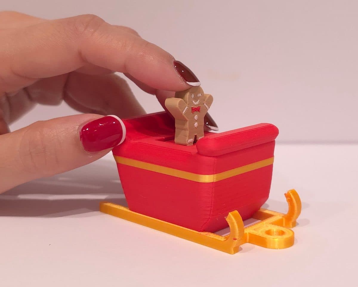 A hand pressing the gingerbread man down into the red sleigh clicker on its gold runners